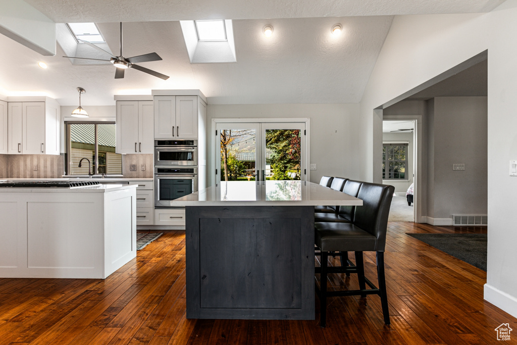 Kitchen featuring white cabinets, vaulted ceiling with skylight, dark hardwood / wood-style floors, and stainless steel double oven