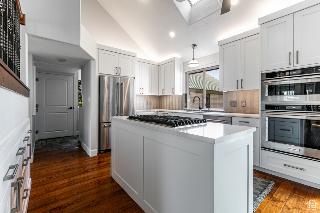 Kitchen featuring appliances with stainless steel finishes, sink, vaulted ceiling with skylight, white cabinets, and dark wood-type flooring