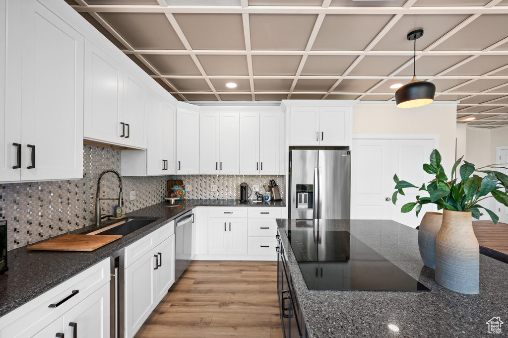 Kitchen featuring backsplash, appliances with stainless steel finishes, dark stone counters, light hardwood / wood-style flooring, and sink