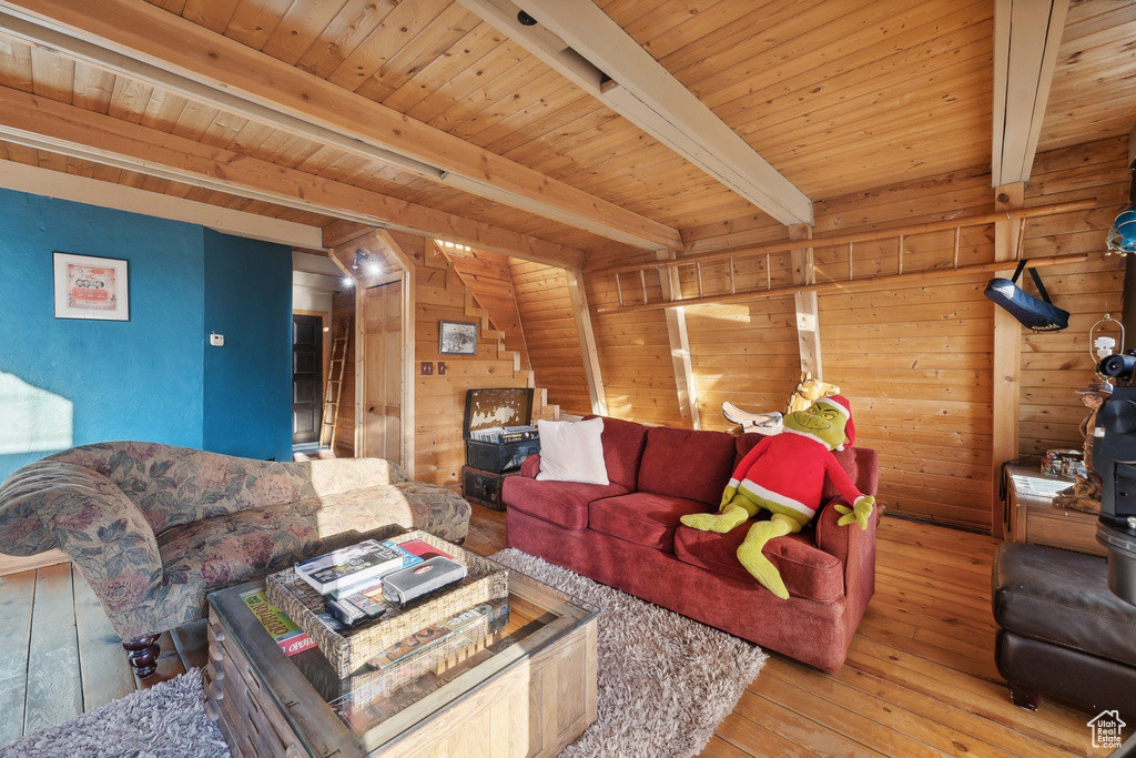 Living room with beam ceiling, wooden walls, light hardwood / wood-style flooring, and wooden ceiling