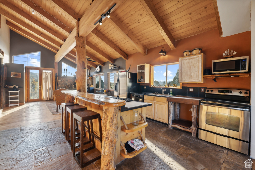 Kitchen with beamed ceiling, stainless steel appliances, light brown cabinetry, and a kitchen island