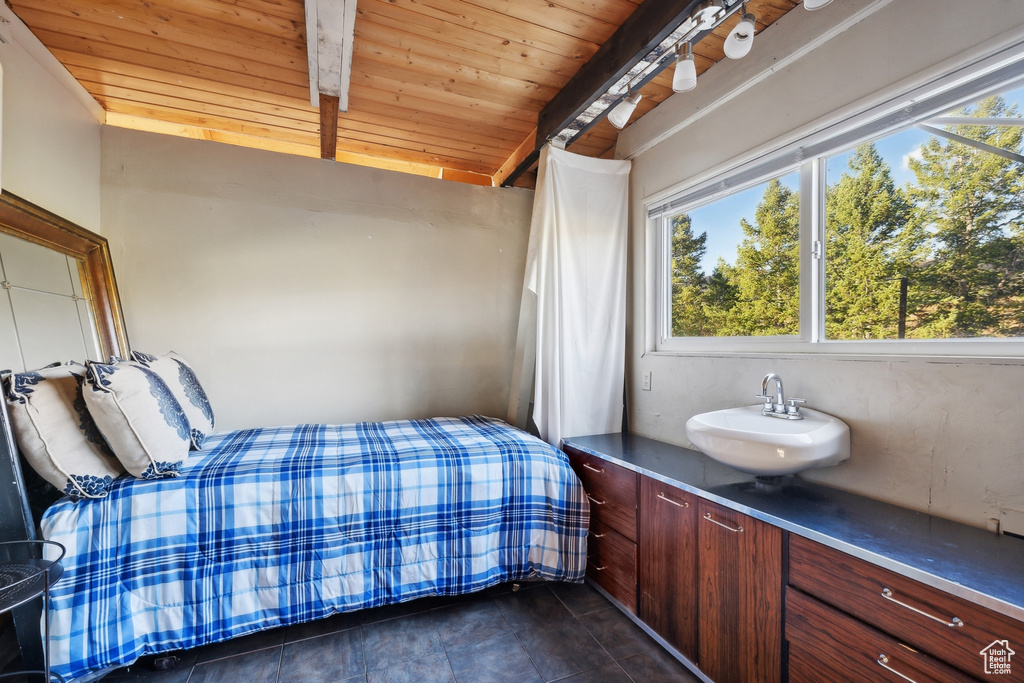 Bedroom featuring beamed ceiling, dark tile patterned floors, sink, and wooden ceiling