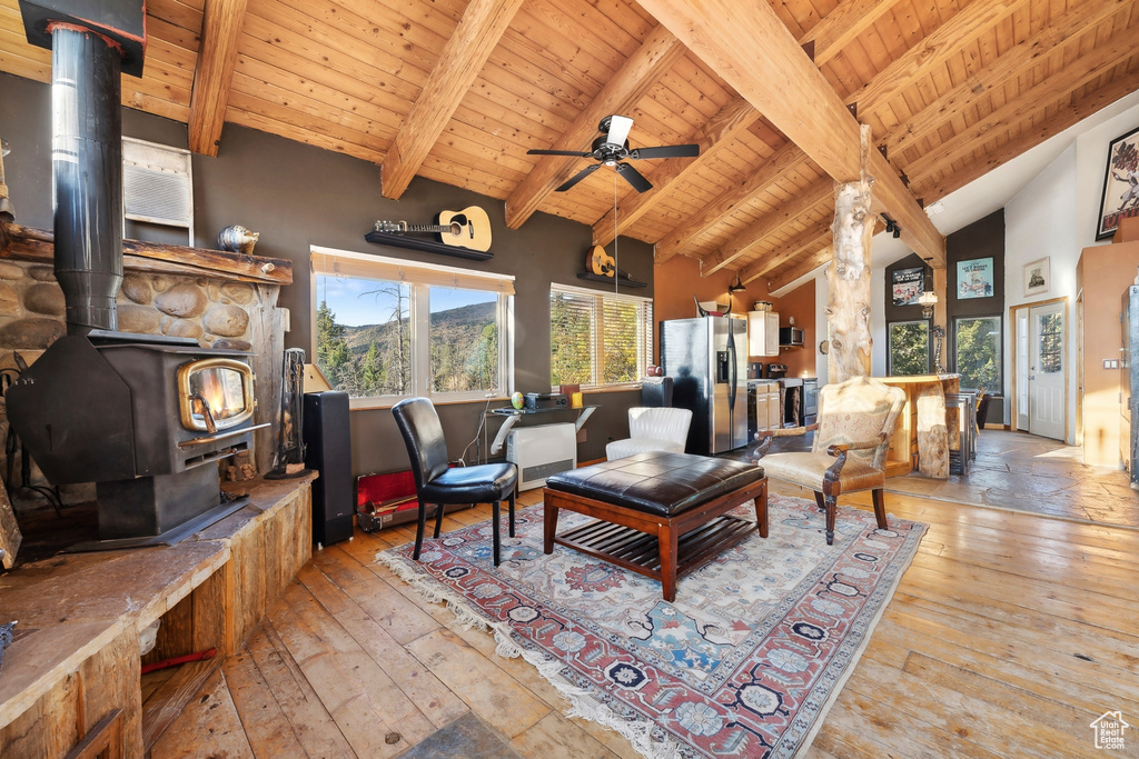 Living room featuring light hardwood / wood-style floors, a wood stove, beamed ceiling, and wood ceiling