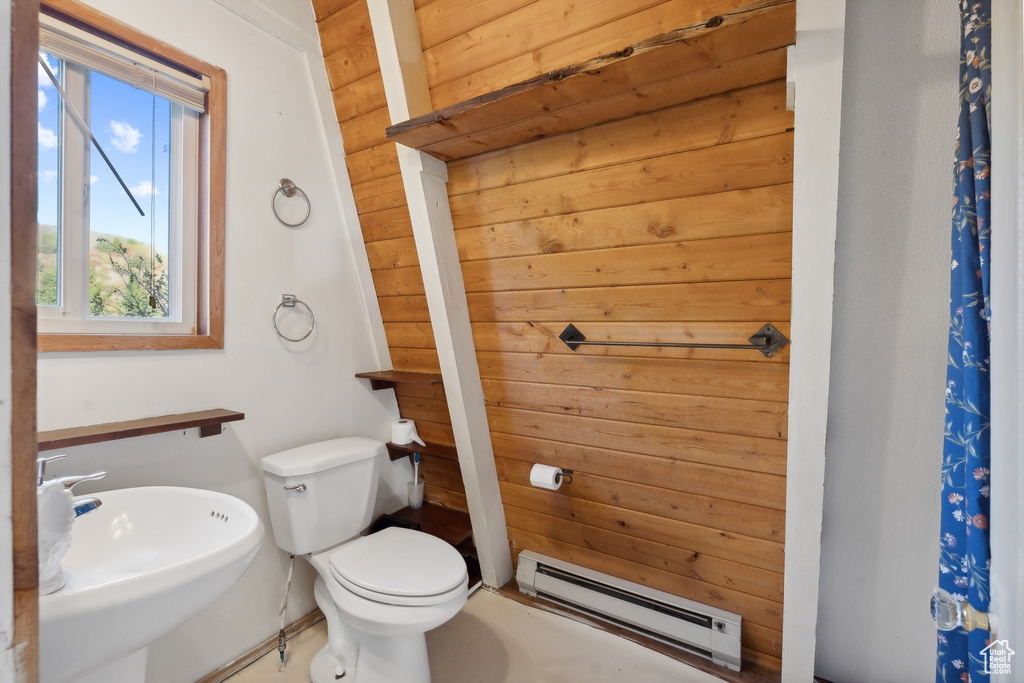 Bathroom with a baseboard radiator, sink, toilet, and wooden walls