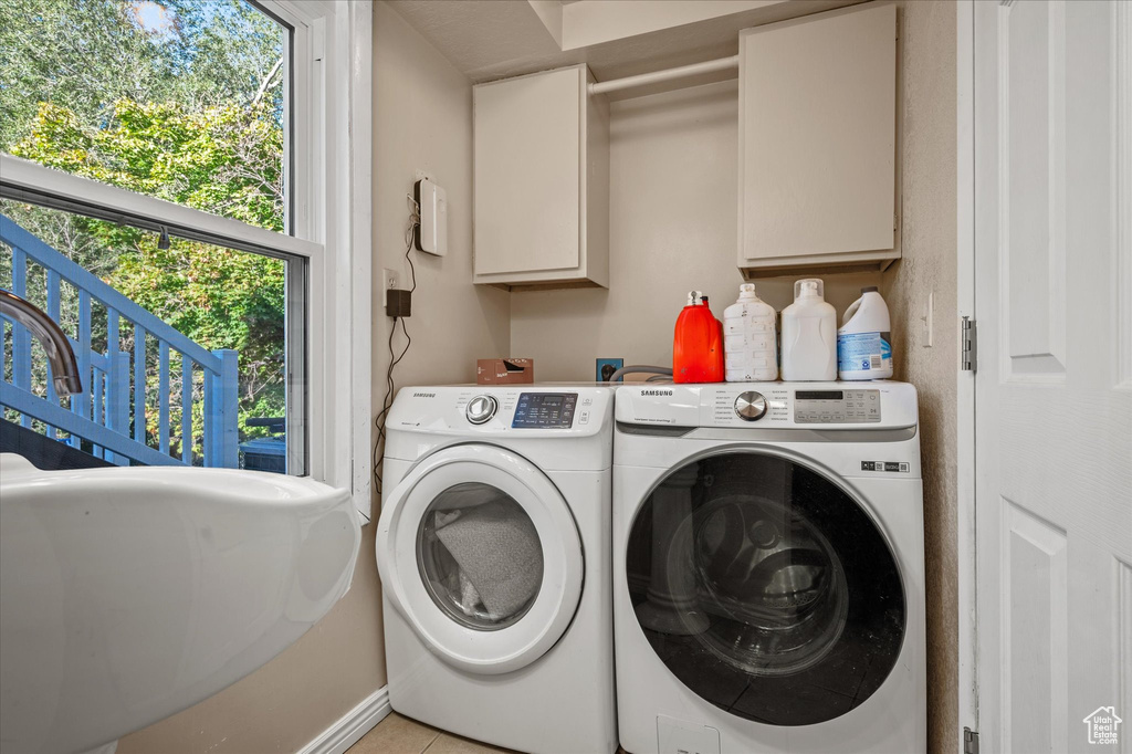 Washroom with washing machine and dryer, light tile patterned floors, and cabinets