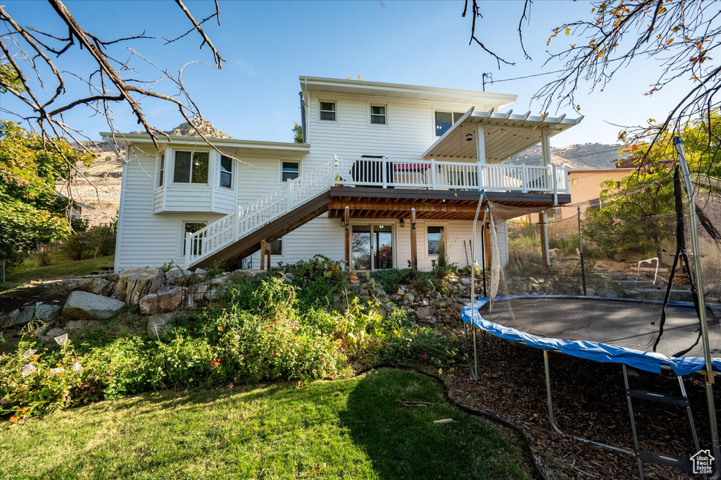 Rear view of house featuring a yard, a deck, and a trampoline