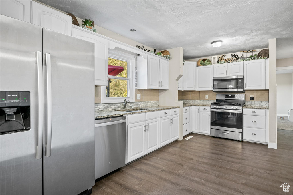 Kitchen with stainless steel appliances, sink, light stone countertops, white cabinets, and dark hardwood / wood-style flooring