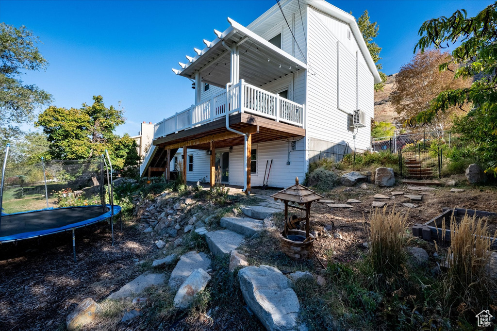 Rear view of house with a deck, cooling unit, and a trampoline