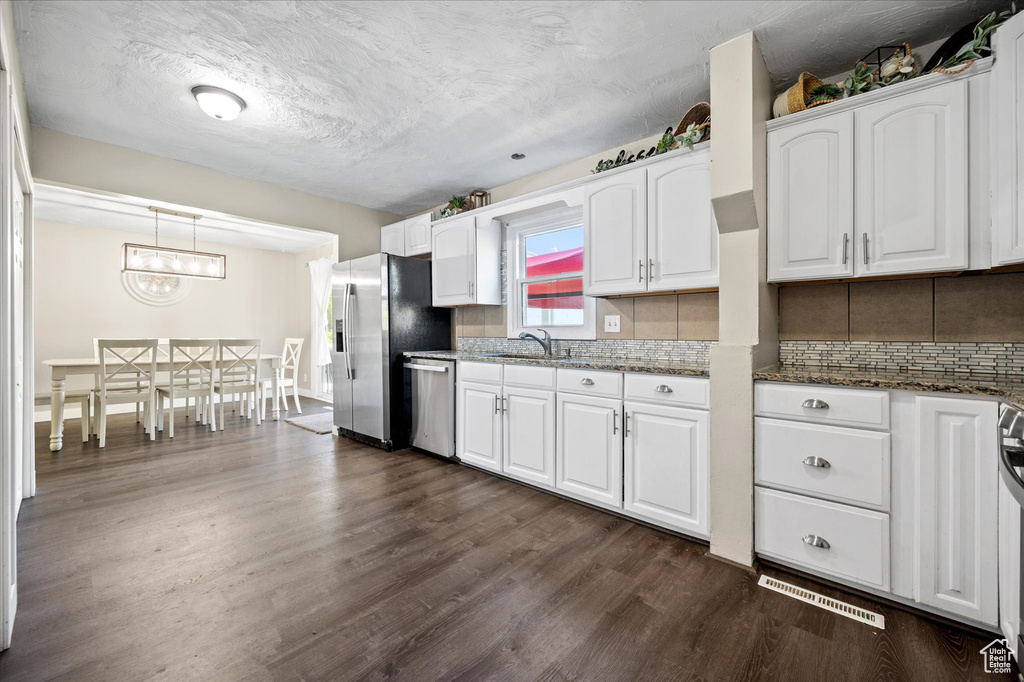 Kitchen with white cabinetry, dark stone countertops, dark wood-type flooring, decorative light fixtures, and stainless steel appliances