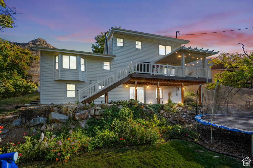 Back house at dusk featuring a wooden deck, a trampoline, and a pergola