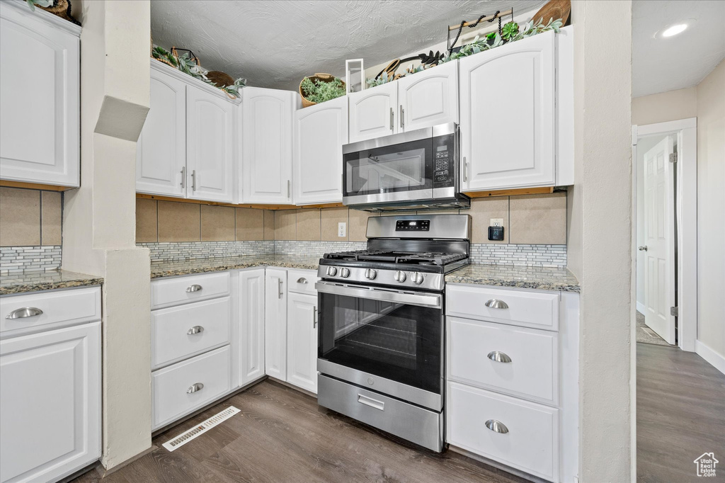 Kitchen with decorative backsplash, white cabinets, stainless steel appliances, and dark hardwood / wood-style flooring