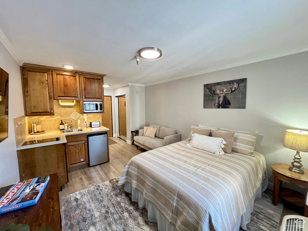 Bedroom with sink, crown molding, light hardwood / wood-style flooring, and stainless steel fridge