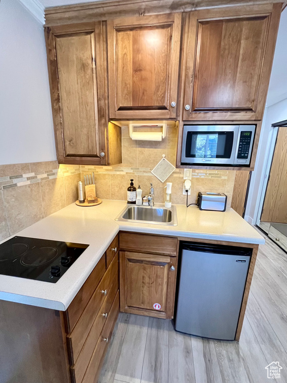 Kitchen featuring sink, appliances with stainless steel finishes, decorative backsplash, and light wood-type flooring