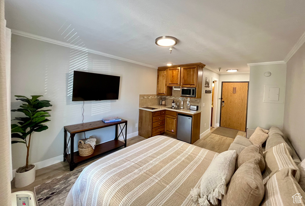 Bedroom featuring ornamental molding, sink, light wood-type flooring, and stainless steel refrigerator