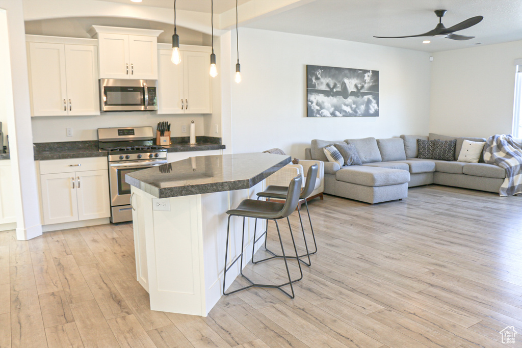 Kitchen with light hardwood / wood-style floors, white cabinets, stainless steel appliances, and hanging light fixtures