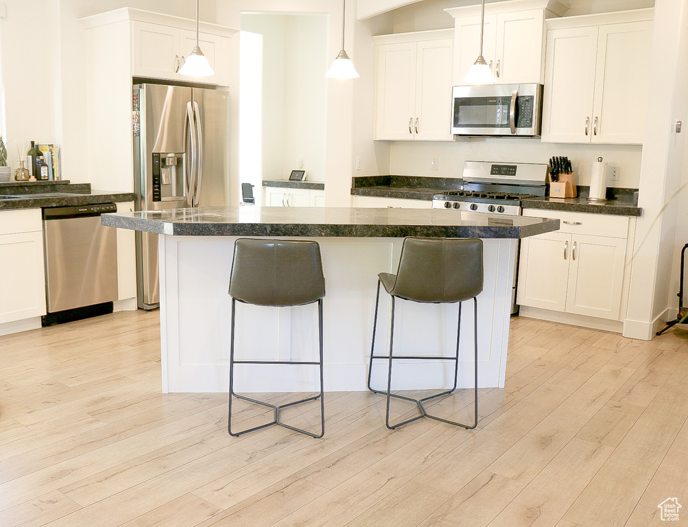 Kitchen featuring white cabinets, appliances with stainless steel finishes, light wood-type flooring, decorative light fixtures, and a center island