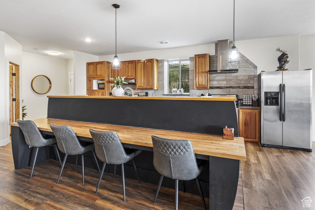 Kitchen with decorative backsplash, wall chimney exhaust hood, stainless steel refrigerator with ice dispenser, and dark hardwood / wood-style floors