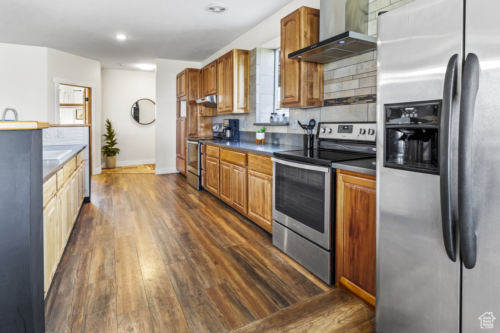 Kitchen with dark wood-type flooring, wall chimney range hood, stainless steel appliances, and backsplash