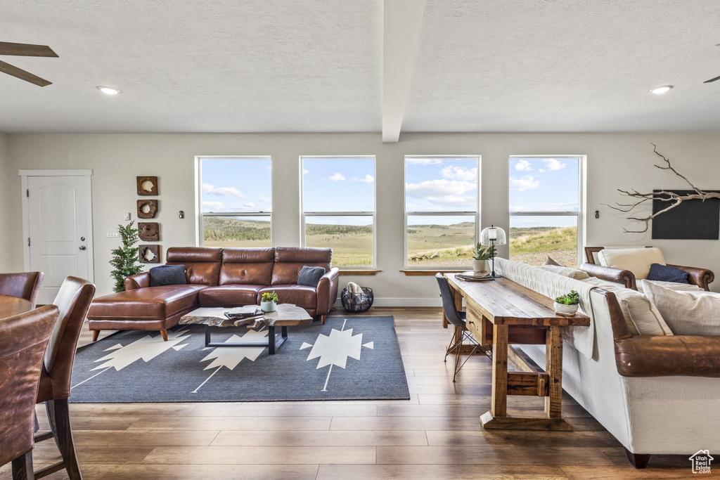 Living room with dark wood-type flooring, ceiling fan, a textured ceiling, and beamed ceiling