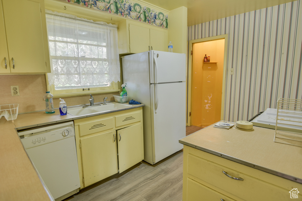 Kitchen with cream cabinetry, sink, light wood-type flooring, and white appliances