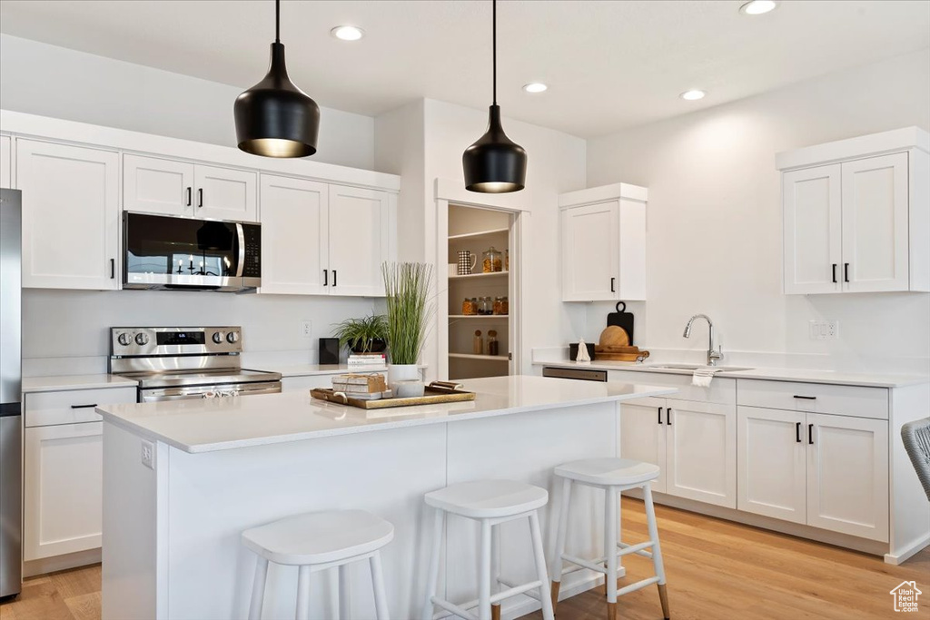 Kitchen featuring hanging light fixtures, appliances with stainless steel finishes, and white cabinets