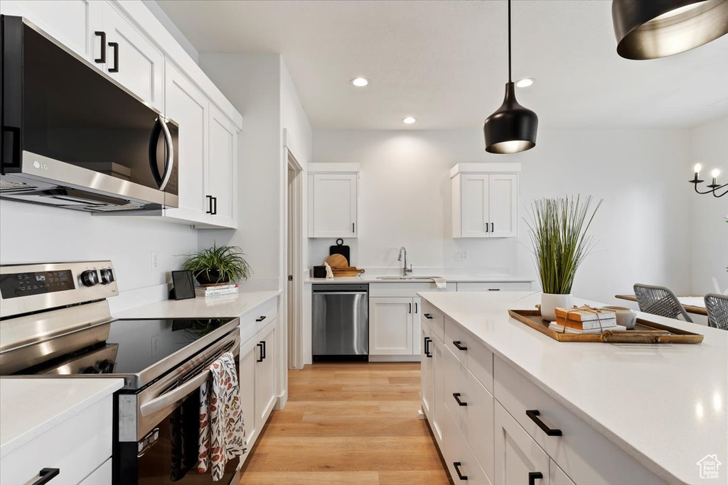 Kitchen with appliances with stainless steel finishes, sink, light hardwood / wood-style floors, decorative light fixtures, and white cabinets