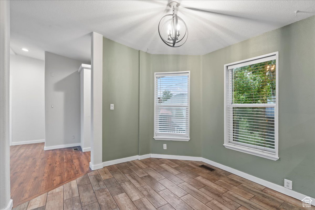 Unfurnished room with hardwood / wood-style floors, a notable chandelier, and a textured ceiling