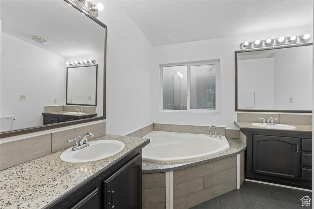 Bathroom featuring vanity, tile patterned flooring, and tiled bath