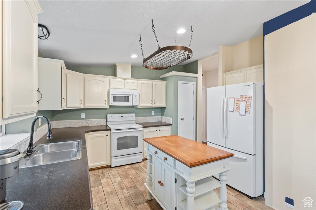 Kitchen featuring white appliances, sink, light wood-type flooring, vaulted ceiling, and white cabinets