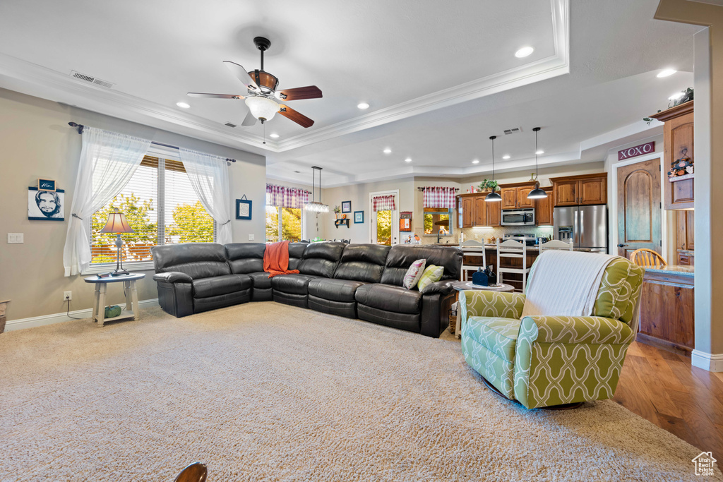 Living room featuring ceiling fan, crown molding, a tray ceiling, and light hardwood / wood-style floors