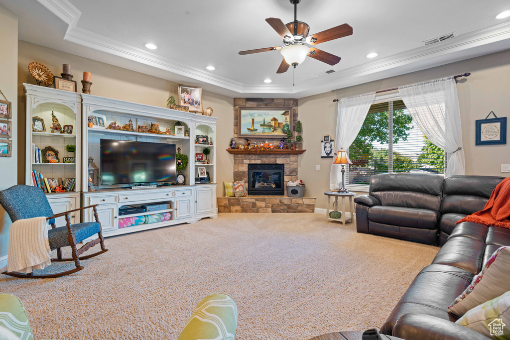 Carpeted living room with a raised ceiling, ornamental molding, a fireplace, and ceiling fan