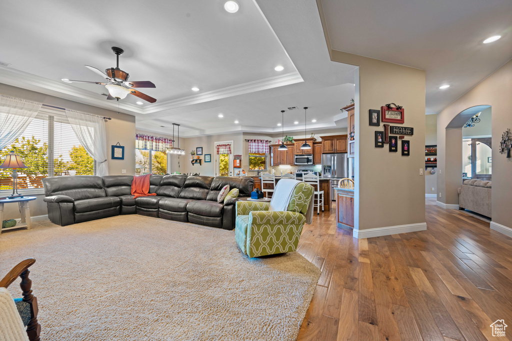 Living room featuring crown molding, light hardwood / wood-style flooring, a tray ceiling, and ceiling fan