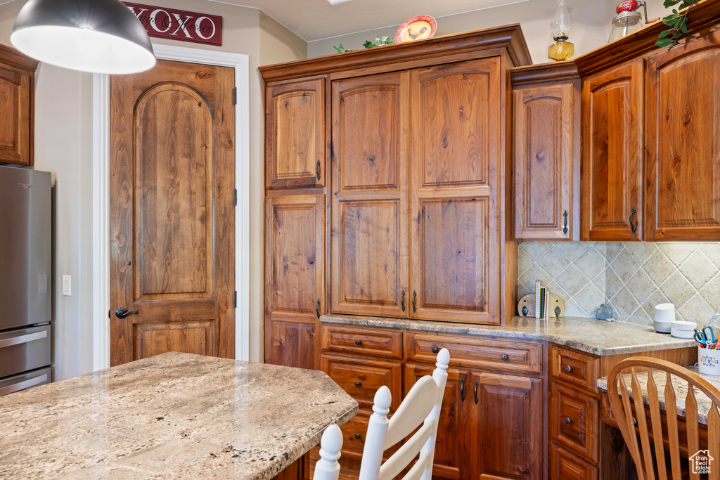 Kitchen with backsplash, light stone countertops, and stainless steel fridge