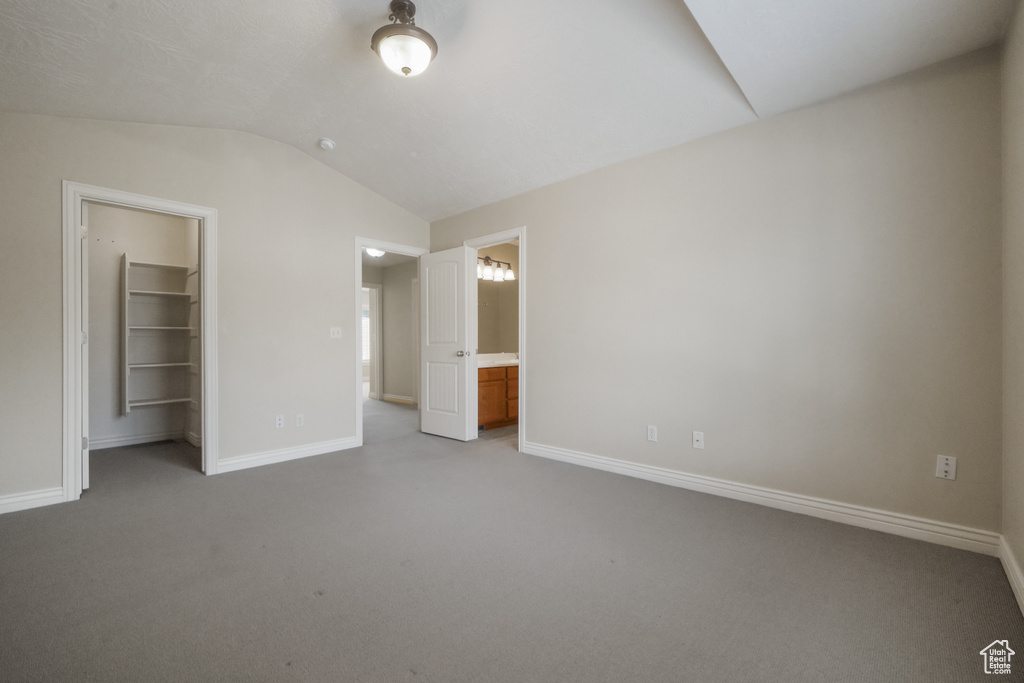 Unfurnished bedroom with a walk in closet, ensuite bath, a closet, vaulted ceiling, and light colored carpet