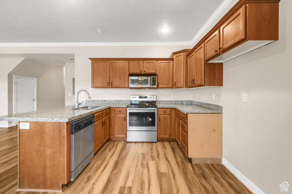 Kitchen featuring appliances with stainless steel finishes, sink, kitchen peninsula, light stone counters, and light hardwood / wood-style flooring