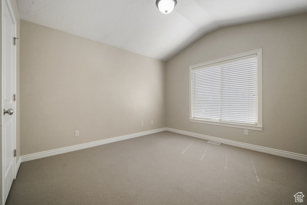 Carpeted spare room featuring vaulted ceiling