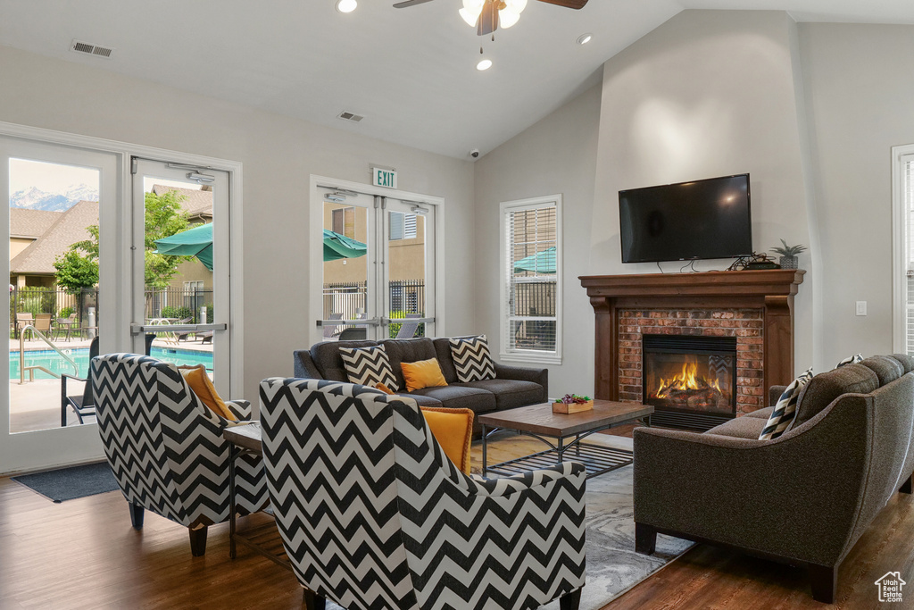 Living room featuring high vaulted ceiling, a healthy amount of sunlight, dark hardwood / wood-style flooring, and a brick fireplace