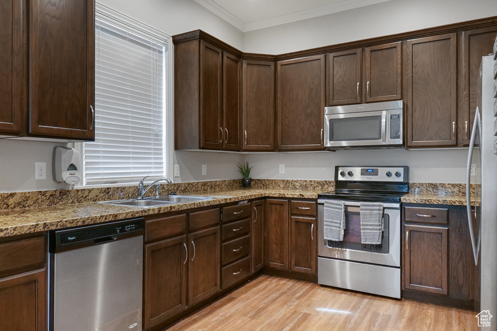 Kitchen with light stone countertops, light hardwood / wood-style flooring, ornamental molding, dark brown cabinetry, and stainless steel appliances