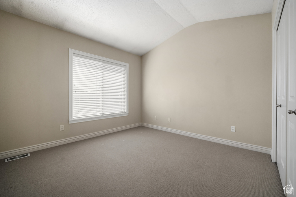 Carpeted empty room featuring vaulted ceiling