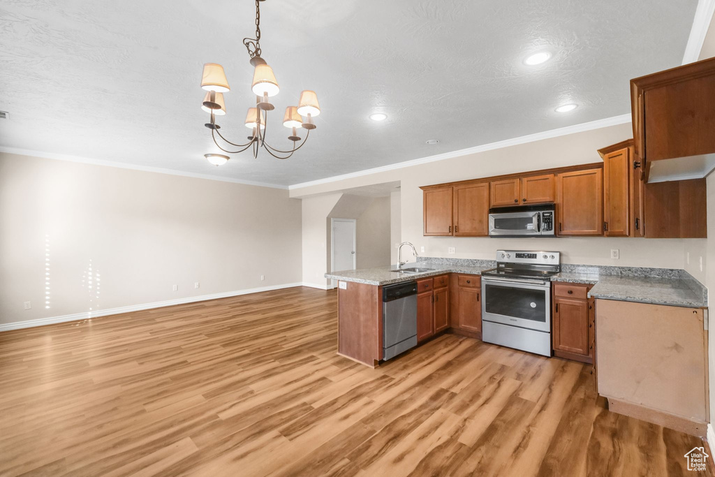 Kitchen featuring hanging light fixtures, appliances with stainless steel finishes, a chandelier, light hardwood / wood-style flooring, and crown molding