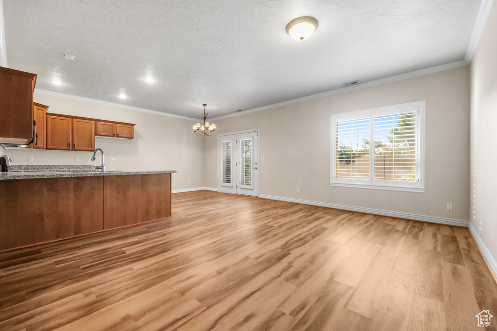 Kitchen with a wealth of natural light, light hardwood / wood-style flooring, a notable chandelier, and light stone countertops