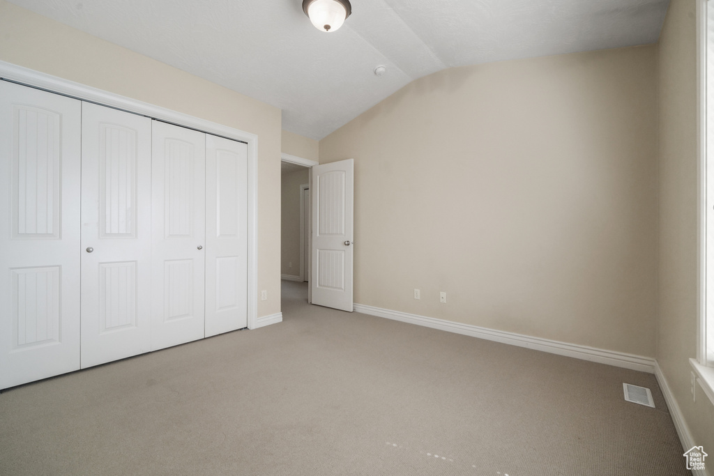 Unfurnished bedroom featuring vaulted ceiling, light colored carpet, and a closet