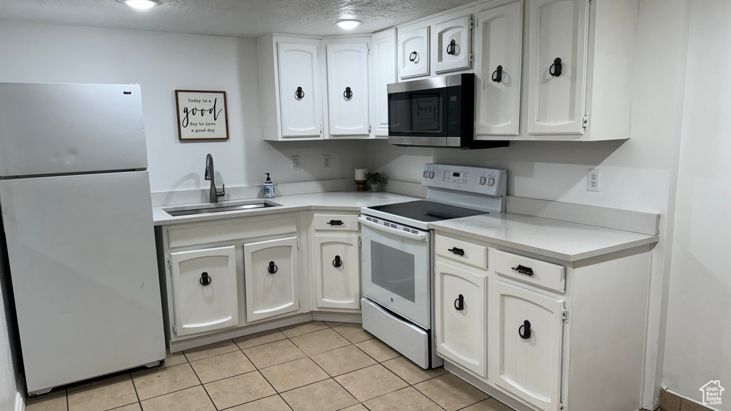 Kitchen featuring white cabinets, sink, light tile patterned floors, and white appliances