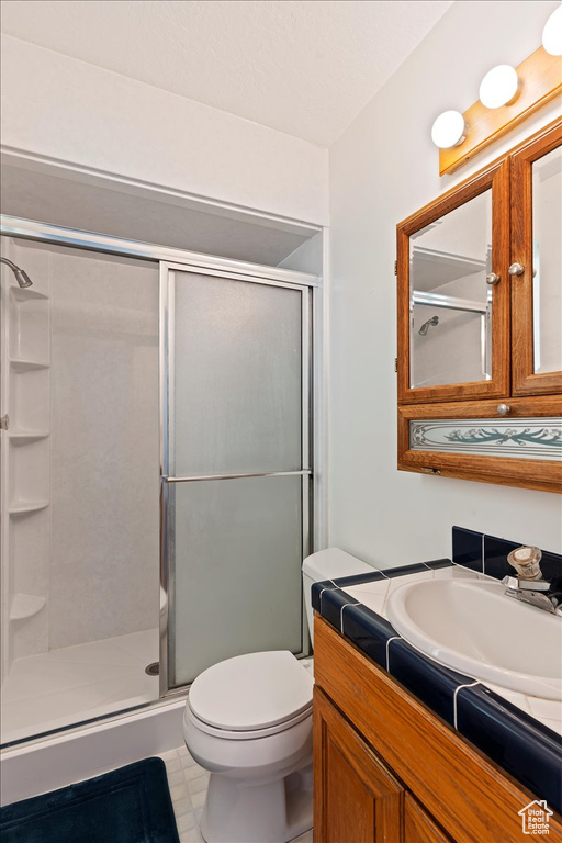 Bathroom featuring a shower with door, vanity, toilet, and tile patterned flooring