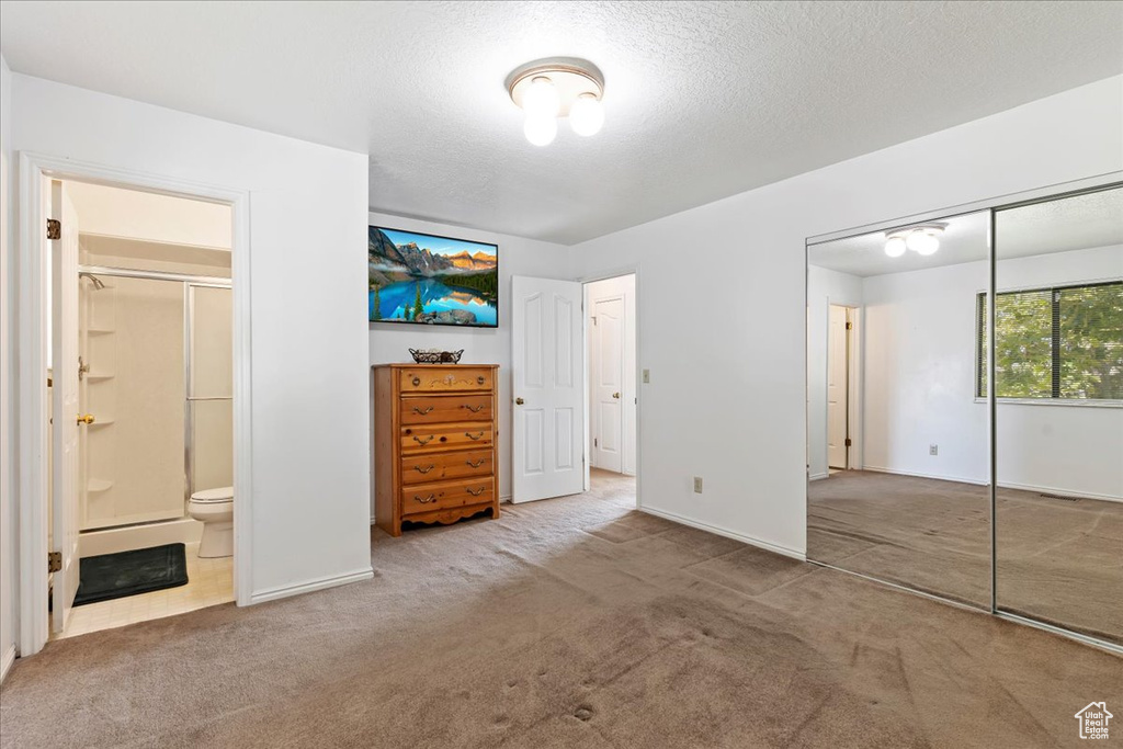 Unfurnished bedroom with a closet, light carpet, a textured ceiling, and ensuite bathroom