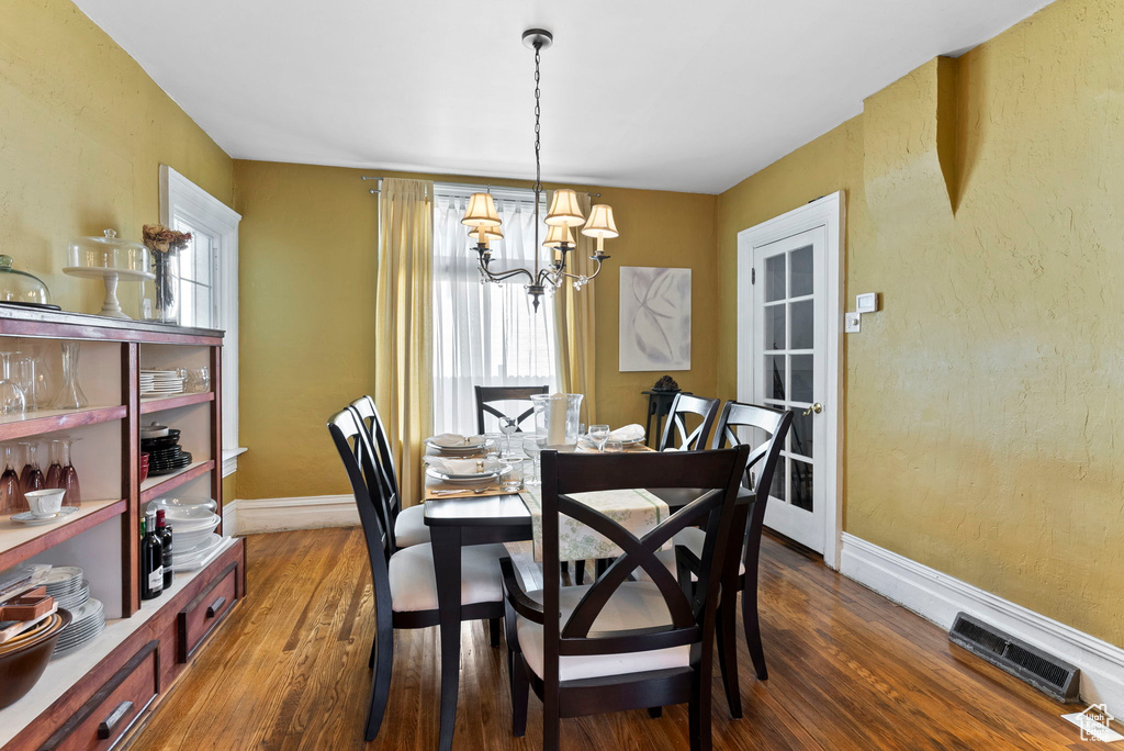 Dining space with a healthy amount of sunlight, dark hardwood / wood-style flooring, and a chandelier