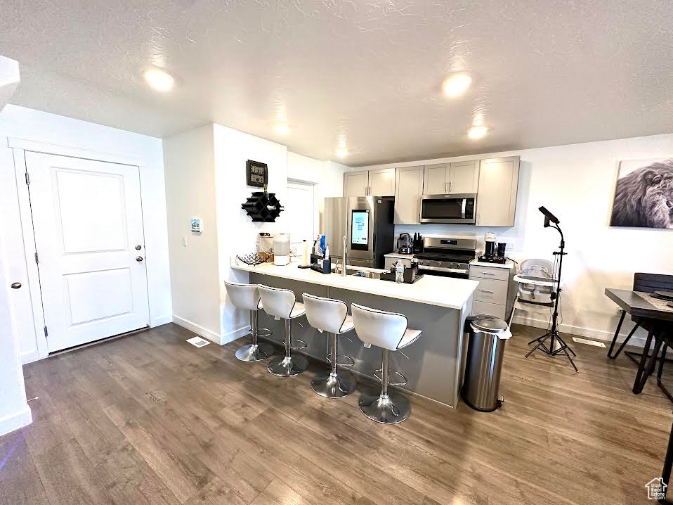 Kitchen with appliances with stainless steel finishes, a kitchen bar, dark hardwood / wood-style flooring, kitchen peninsula, and gray cabinets