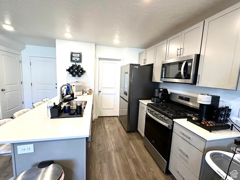 Kitchen featuring a kitchen breakfast bar, light hardwood / wood-style flooring, stainless steel appliances, white cabinets, and a textured ceiling