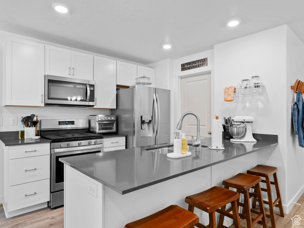 Kitchen featuring a breakfast bar, white cabinetry, sink, light hardwood / wood-style floors, and stainless steel appliances