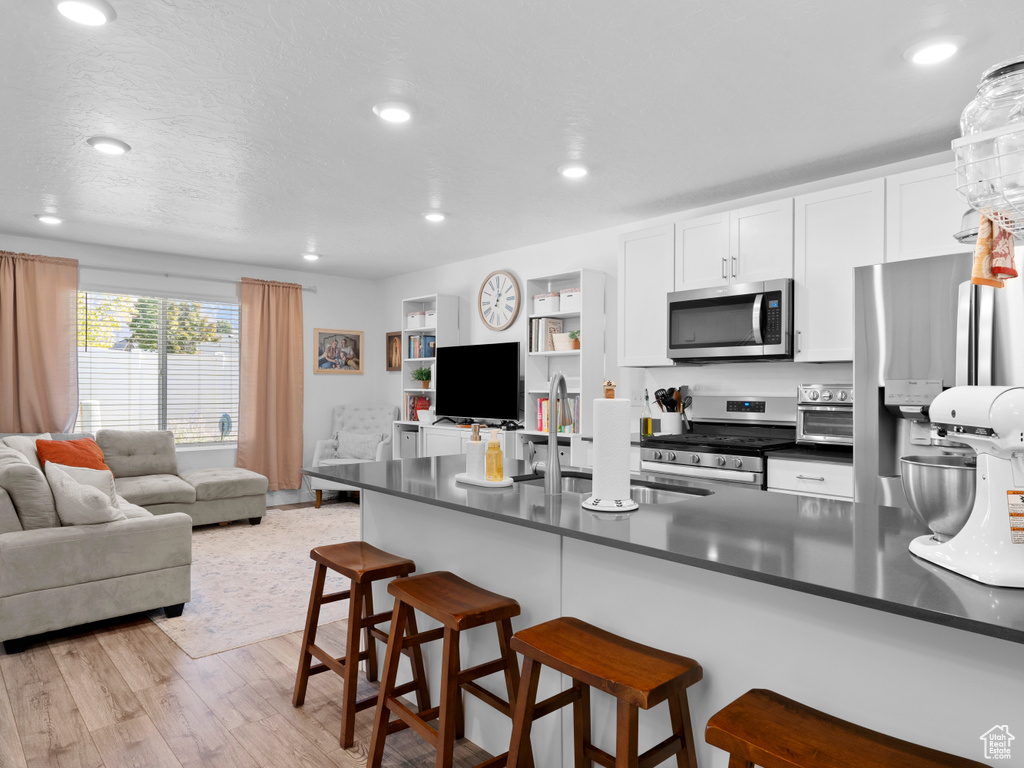 Kitchen featuring appliances with stainless steel finishes, sink, white cabinetry, light hardwood / wood-style floors, and a breakfast bar